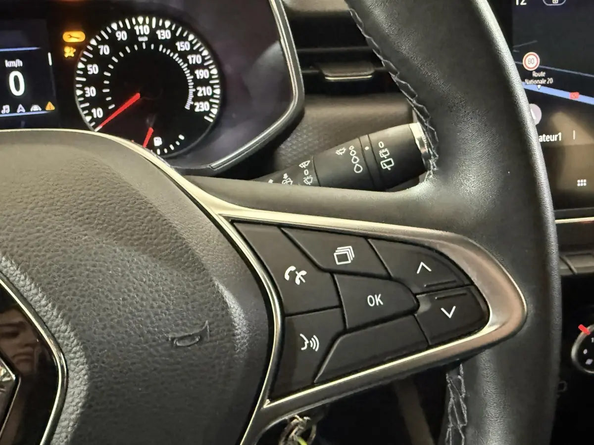 Gros plan sur le volant cuir synthétique de la Renault Clio Business blanc 2021 avec commandes multifonctions et tableau de bord numérique.