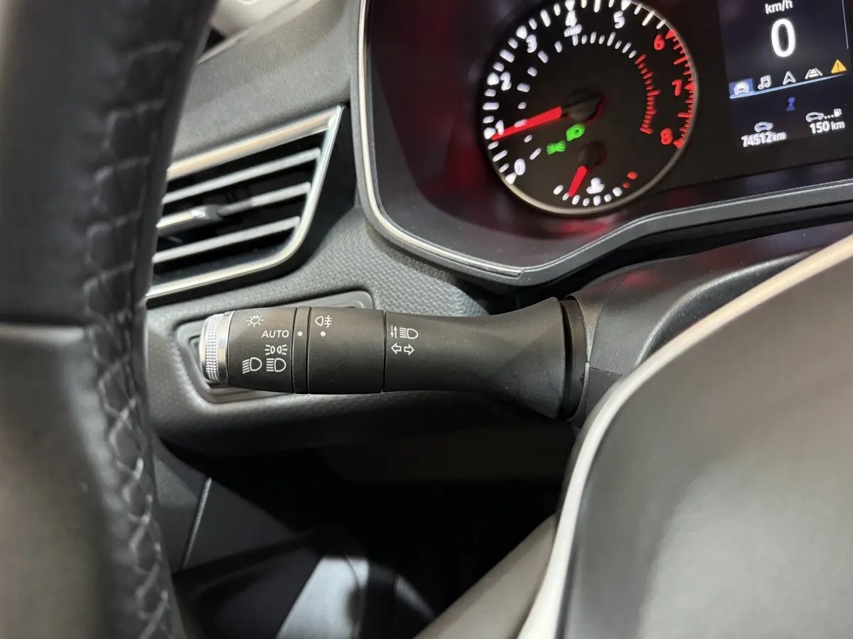 Gros plan sur la manette des feux et clignotants à gauche du volant cuir synthétique dans le tableau de bord de la Renault Clio blanche.