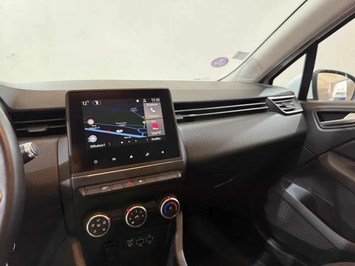 Vue intérieure côté passager de la Renault Clio Business blanche, avec écran tactile de navigation et commandes de climatisation.