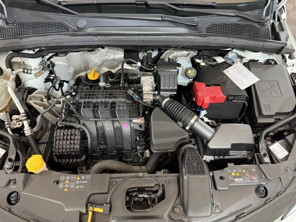 Vue plongeante sur le moteur essence d'une Renault Clio Business blanche de 2021 avec batterie et durites visibles.