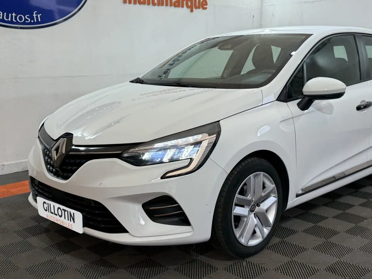 Renault Clio Business blanche vue 3/4 avant droit, avec phares LED allumés et jantes alliage visibles.
