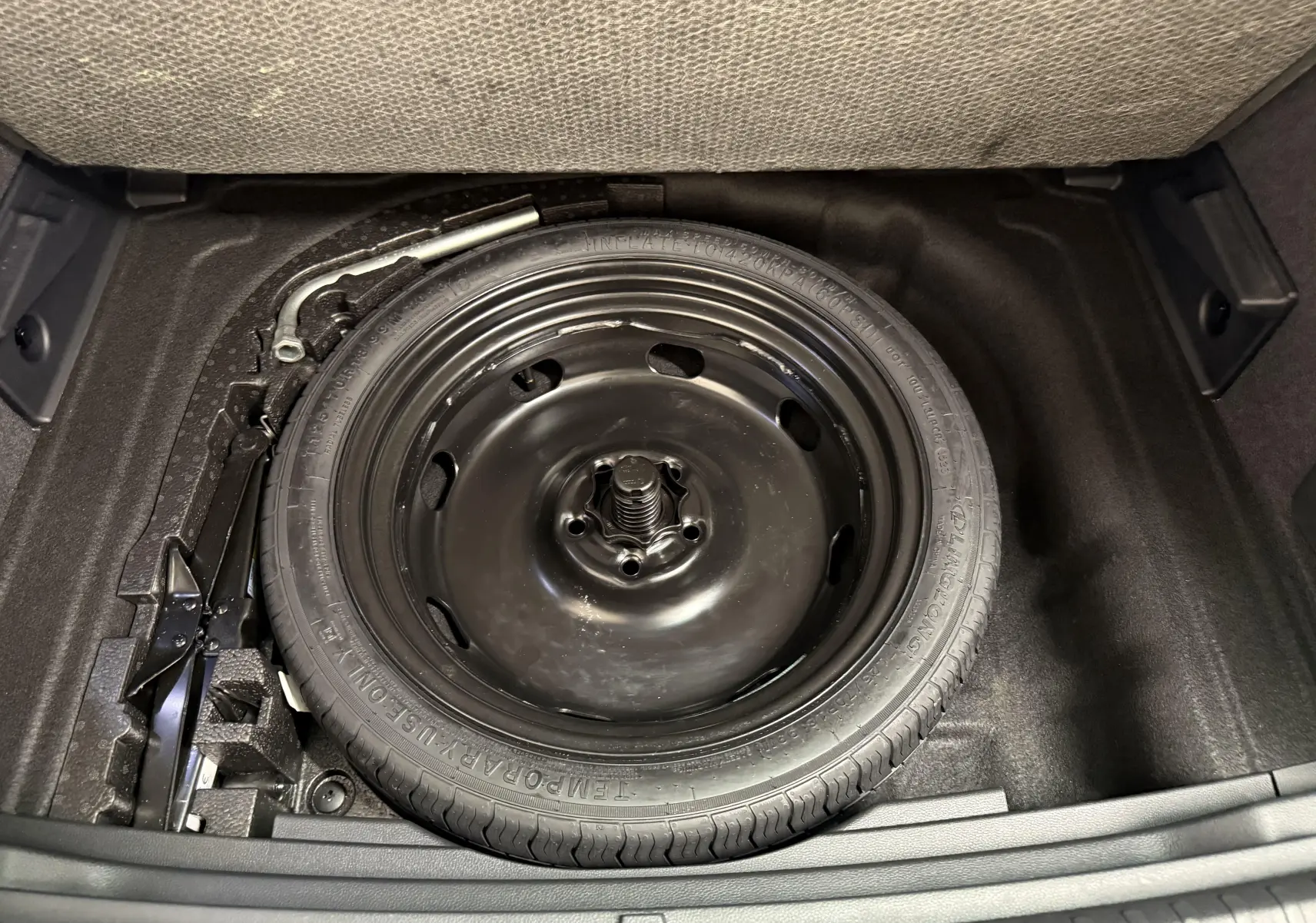 Gros plan sur la roue de secours compacte 18'' noire dans le coffre à double fond du SEAT Ateca Blanc Nevada 2023.