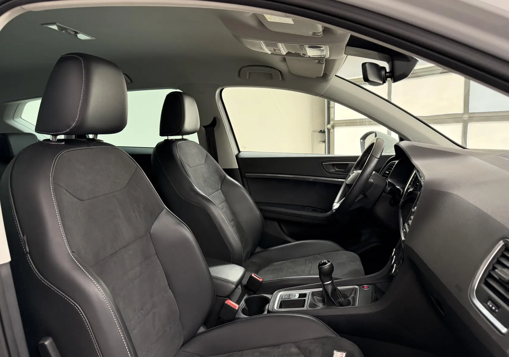 Vue intérieure côté conducteur du SEAT Ateca 2023, sièges noirs en cuir et alcantara avec surpiqûres blanches.