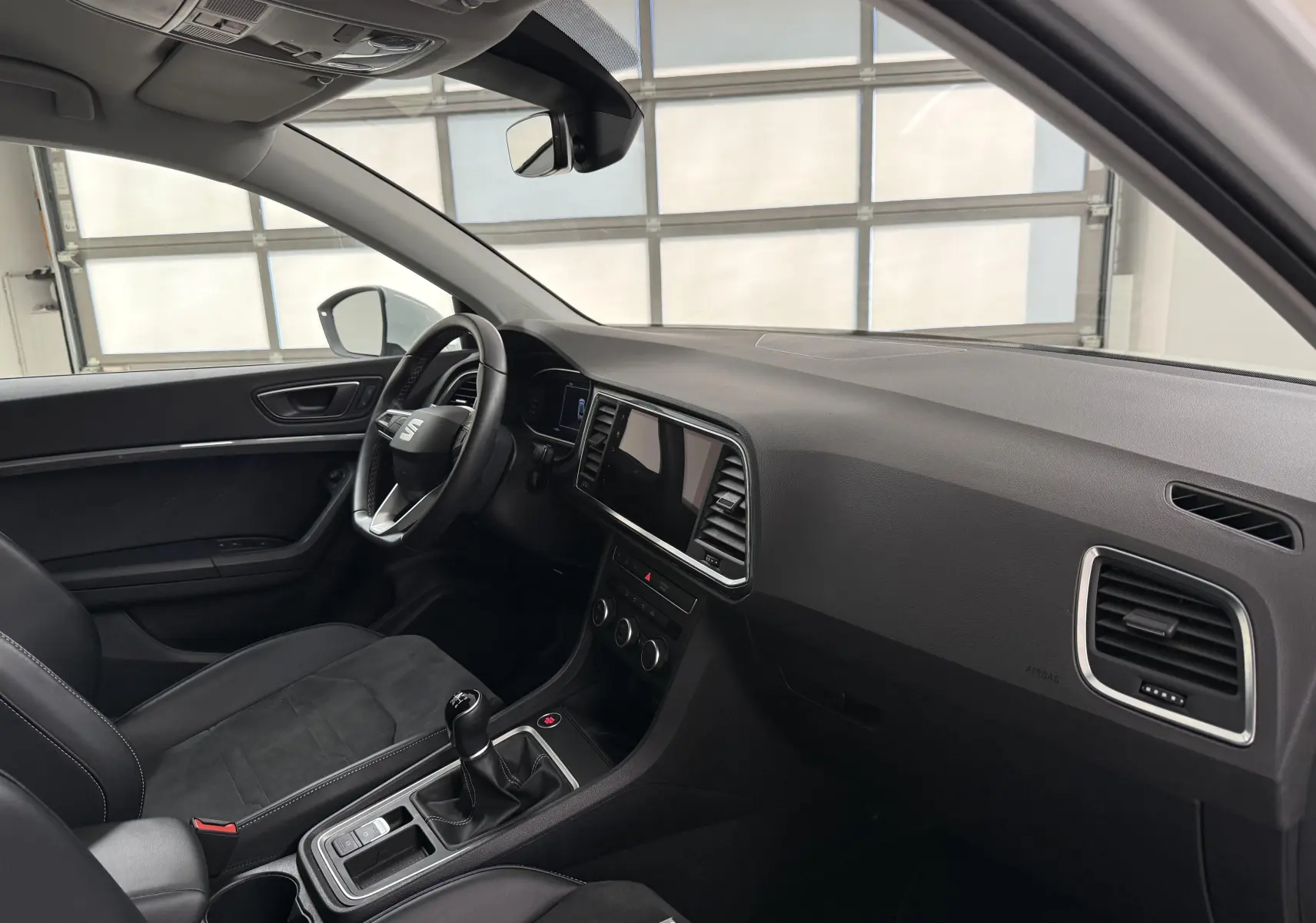 Vue intérieure côté conducteur du SEAT Ateca 2023, tableau de bord noir avec boîte manuelle et écran tactile central.