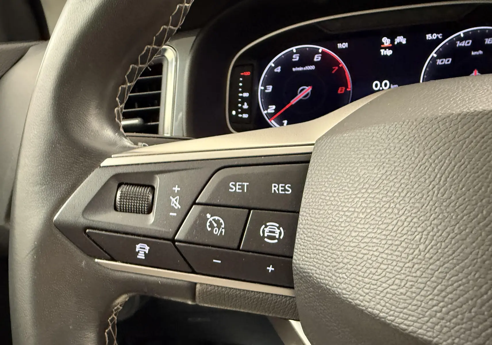Gros plan sur les commandes au volant gauche du SEAT Ateca blanc Nevada, avec tableau de bord numérique en arrière-plan.