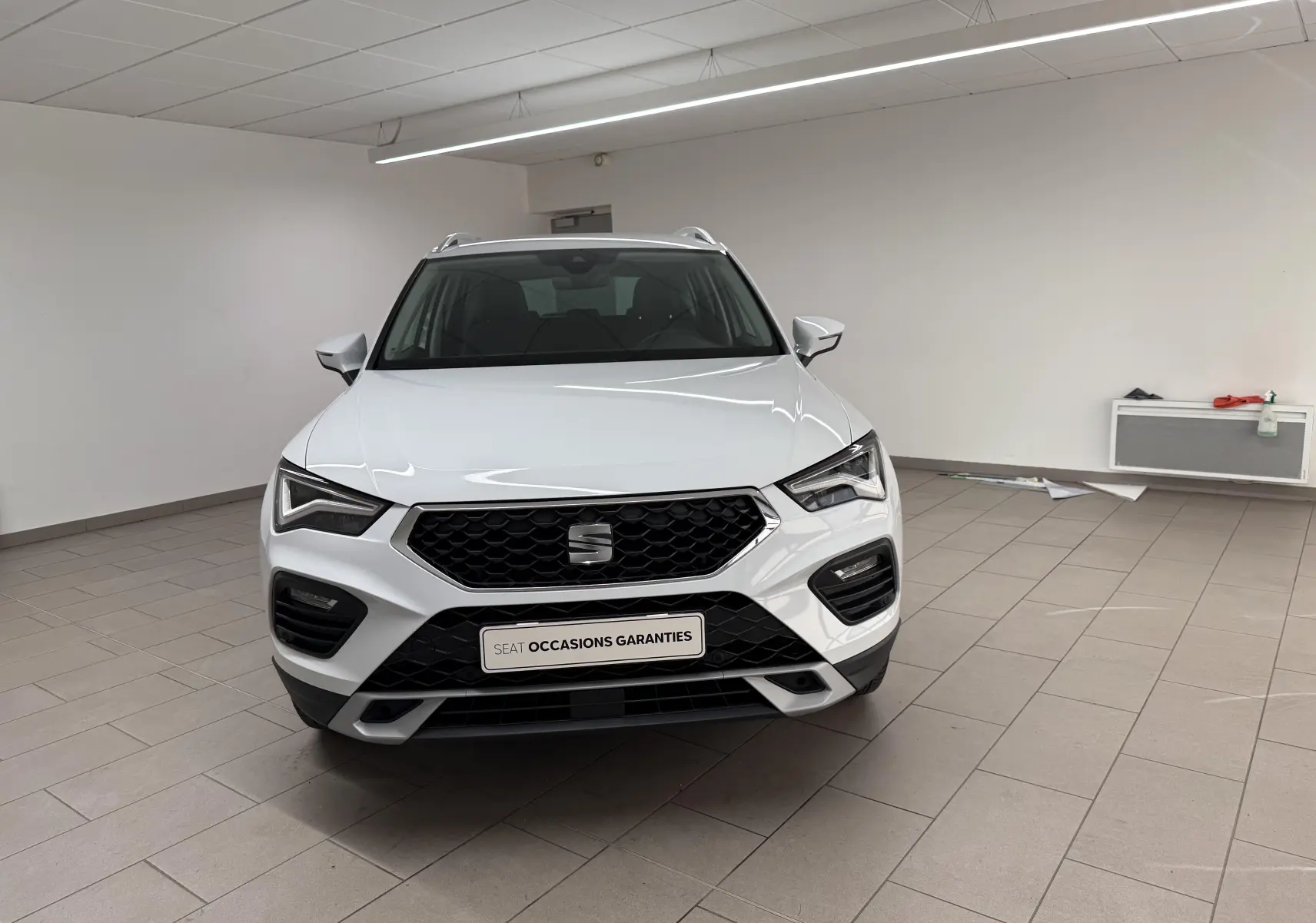 Vue avant d'un SEAT Ateca blanc Nevada 2023 dans un showroom, avec calandre noire et feux LED distinctifs.