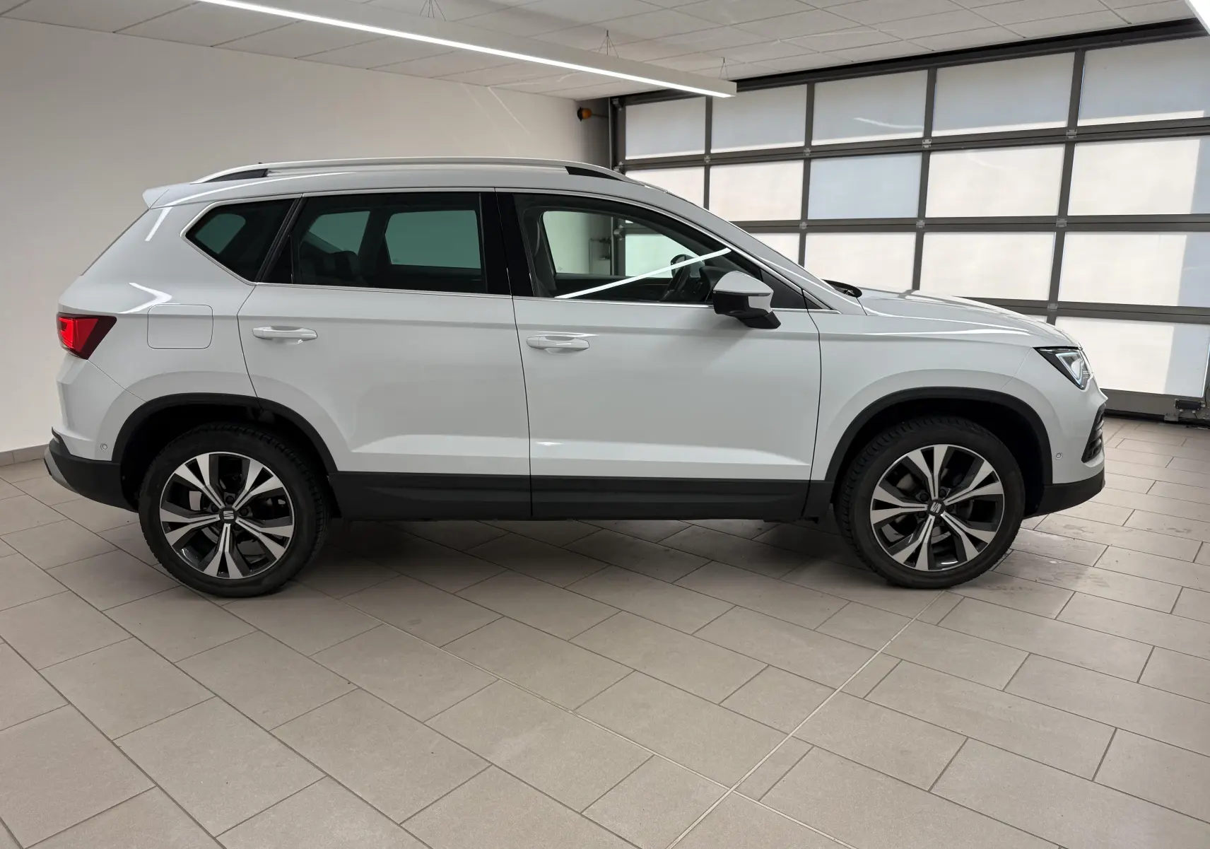 Vue de profil côté gauche d’un SEAT Ateca 2023 blanc Nevada avec jantes alliage et barres de toit noires.