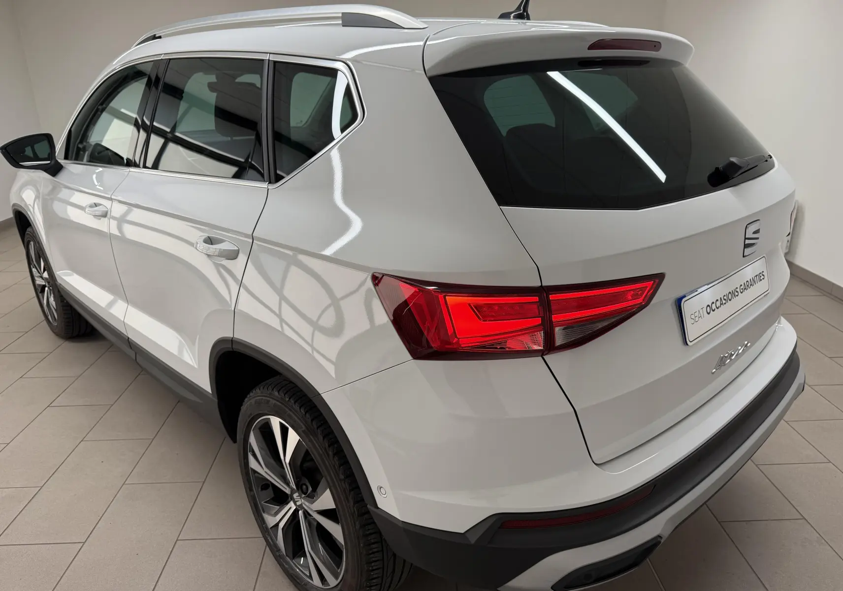 Vue 3/4 arrière droite du SEAT Ateca blanc Nevada 2023 avec feux arrière allumés et jantes alliage bicolores.