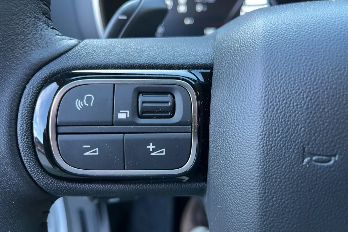 Gros plan sur les commandes gauche du volant en cuir du Citroën C5 Aircross Hybrid blanc, avec boutons de réglage audio et voix.