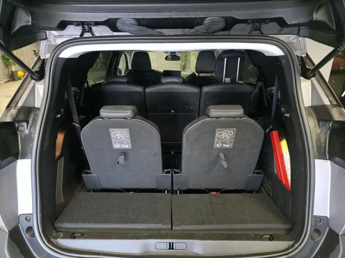 Vue arrière du coffre ouvert d’un Peugeot 5008 gris, montrant les sièges escamotés du troisième rang et l’habitacle noir.