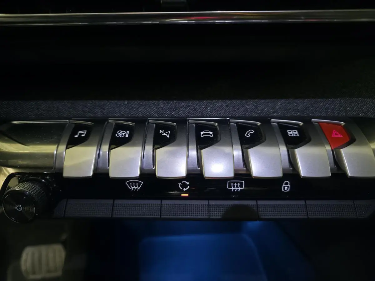 Gros plan sur les commandes en métal brossé de la console centrale du Peugeot 5008 gris, avec éclairage d'ambiance bleu.