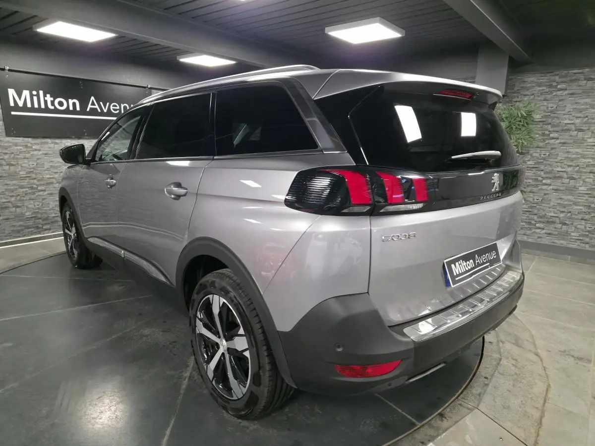 Vue 3/4 arrière droite d’un Peugeot 5008 gris métallisé avec jantes alliage bi-ton et vitres surteintées en intérieur showroom.