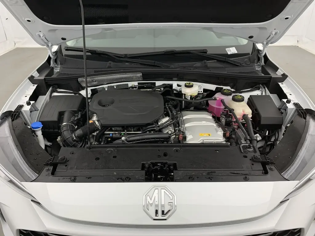 Vue de face sous le capot ouvert du MG ZS Dover White 2026, montrant le moteur hybride et les réservoirs fluides.
