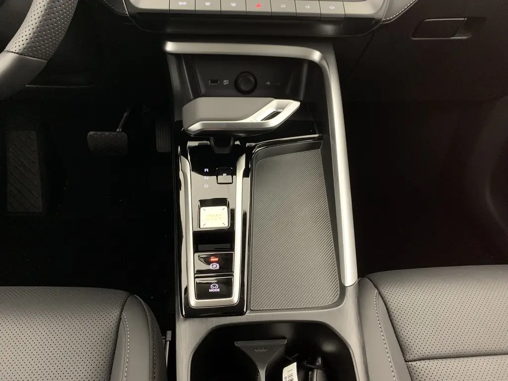 Vue plongeante sur la console centrale noire brillante du MG ZS 1.5 L Hybrid+ avec levier de vitesses et bouton start/stop.