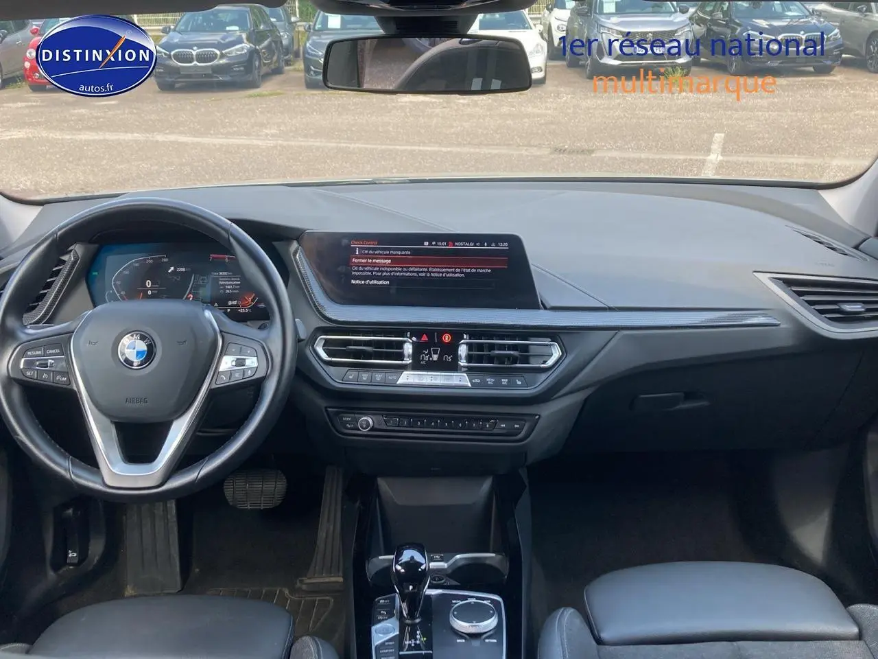 Vue intérieure avant du tableau de bord et volant noir d'une BMW Série 1 gris foncé, avec écran central et console moderne.