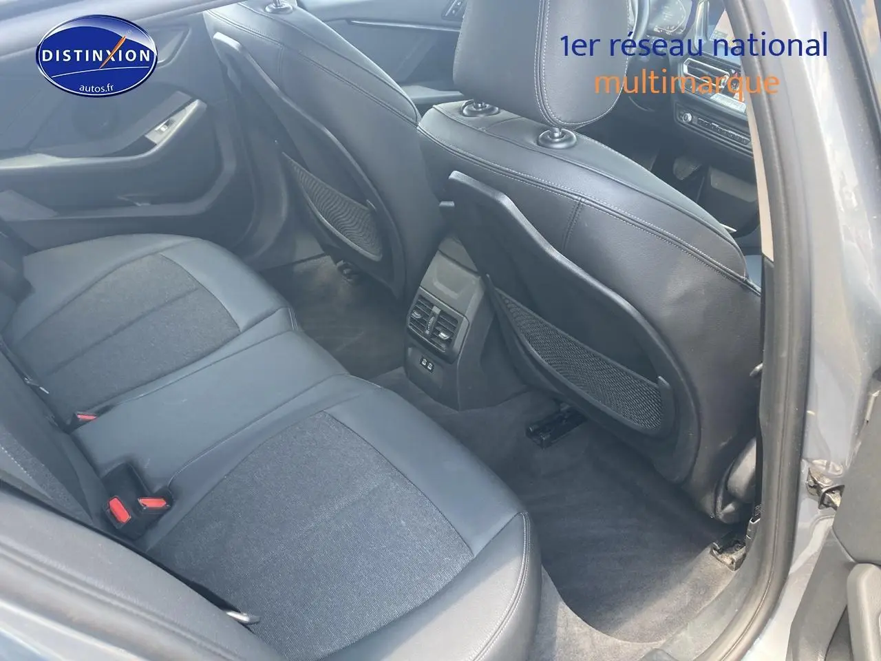 Vue intérieure arrière côté droit de la BMW Série 1 gris foncé, montrant les sièges en tissu et similicuir avec rangements au dos des sièges avant.