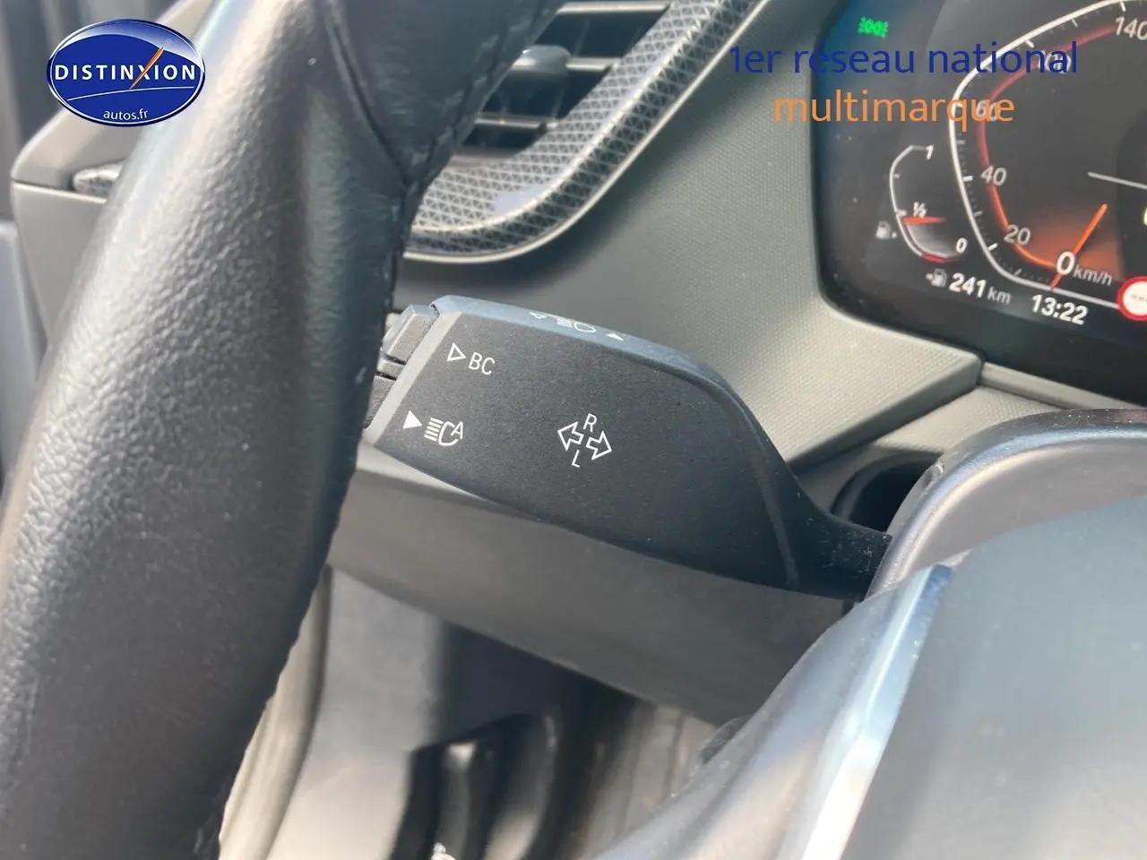 Gros plan sur la commande de clignotant à gauche du volant d’une BMW Série 1 gris foncé, tableau de bord partiellement visible.