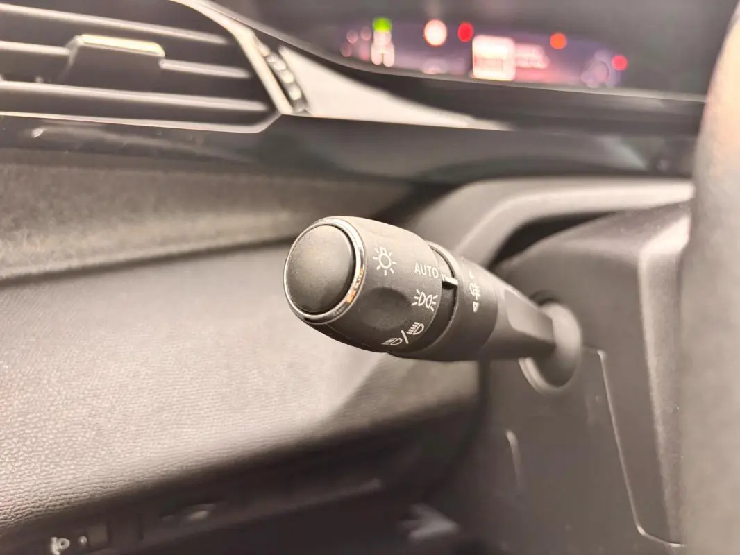 Gros plan sur la commande d’éclairage à gauche du volant dans l’habitacle gris du Peugeot 308 Hybrid 145 e-DCS6 Allure 2025.