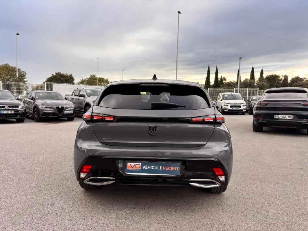 Vue arrière d'une Peugeot 308 Hybrid 145 gris métallisé, avec feux LED allumés et double sortie d'échappement chromée.