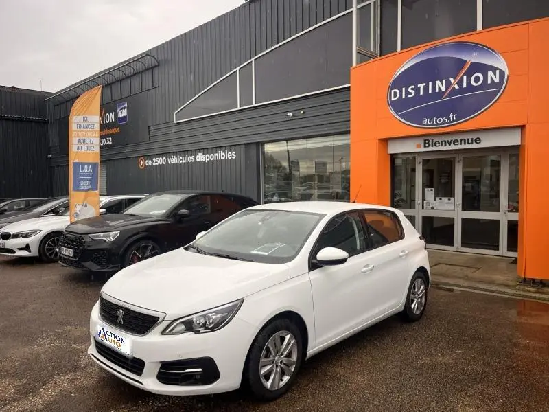 PEUGEOT 308 blanc banquise vue 3/4 avant droit devant un garage avec enseigne orange Distinxion.
