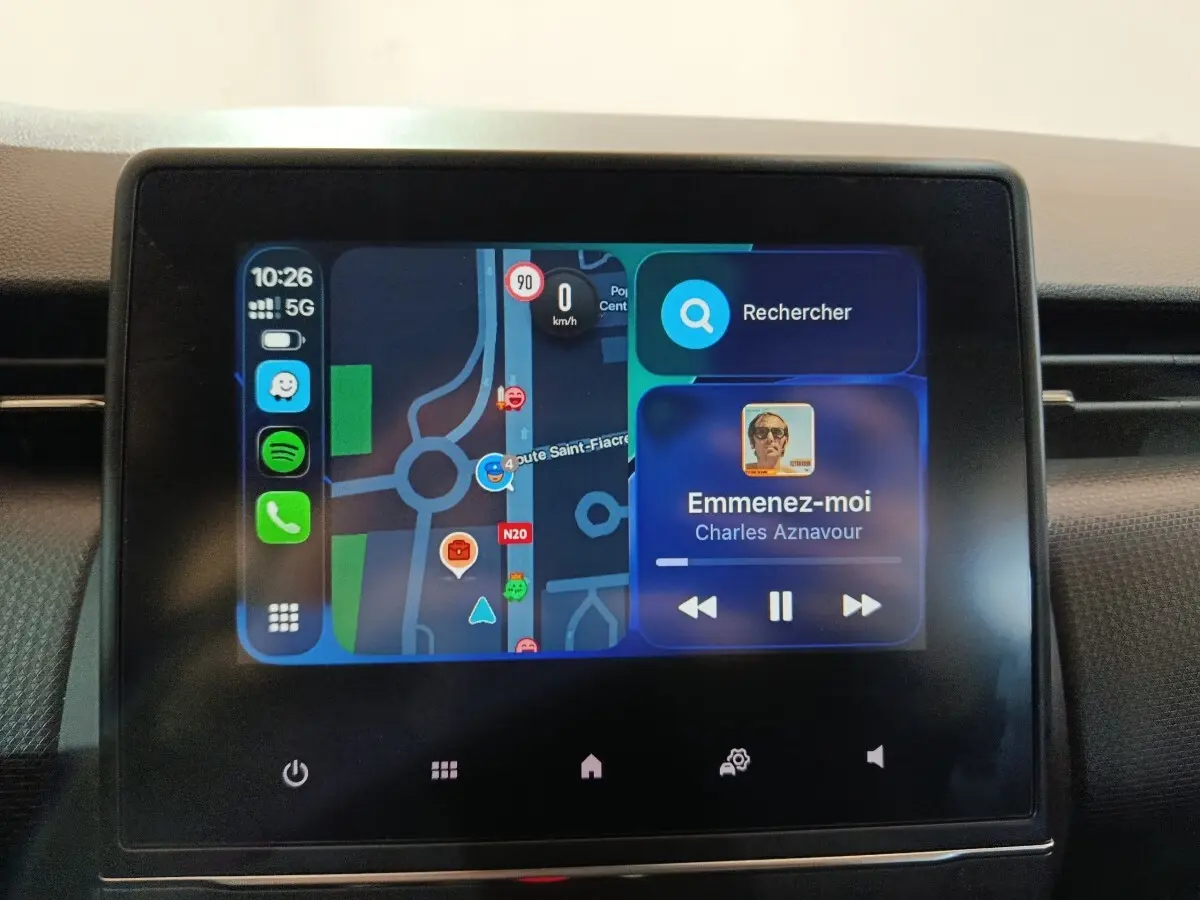 Écran tactile central de la Renault Clio gris clair 2023 affichant navigation et musique en cours de lecture.