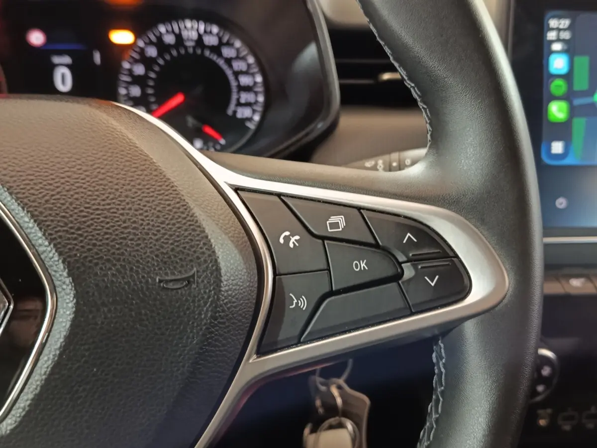 Gros plan sur le volant cuir synthétique noir de la Renault Clio 2023 avec commandes multifonctions et tableau de bord partiel.