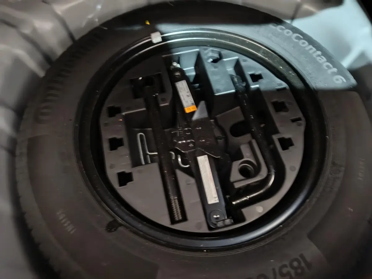 Gros plan sur la roue de secours et ses outils intégrés, sous le coffre d'une Renault Clio gris clair 2023.