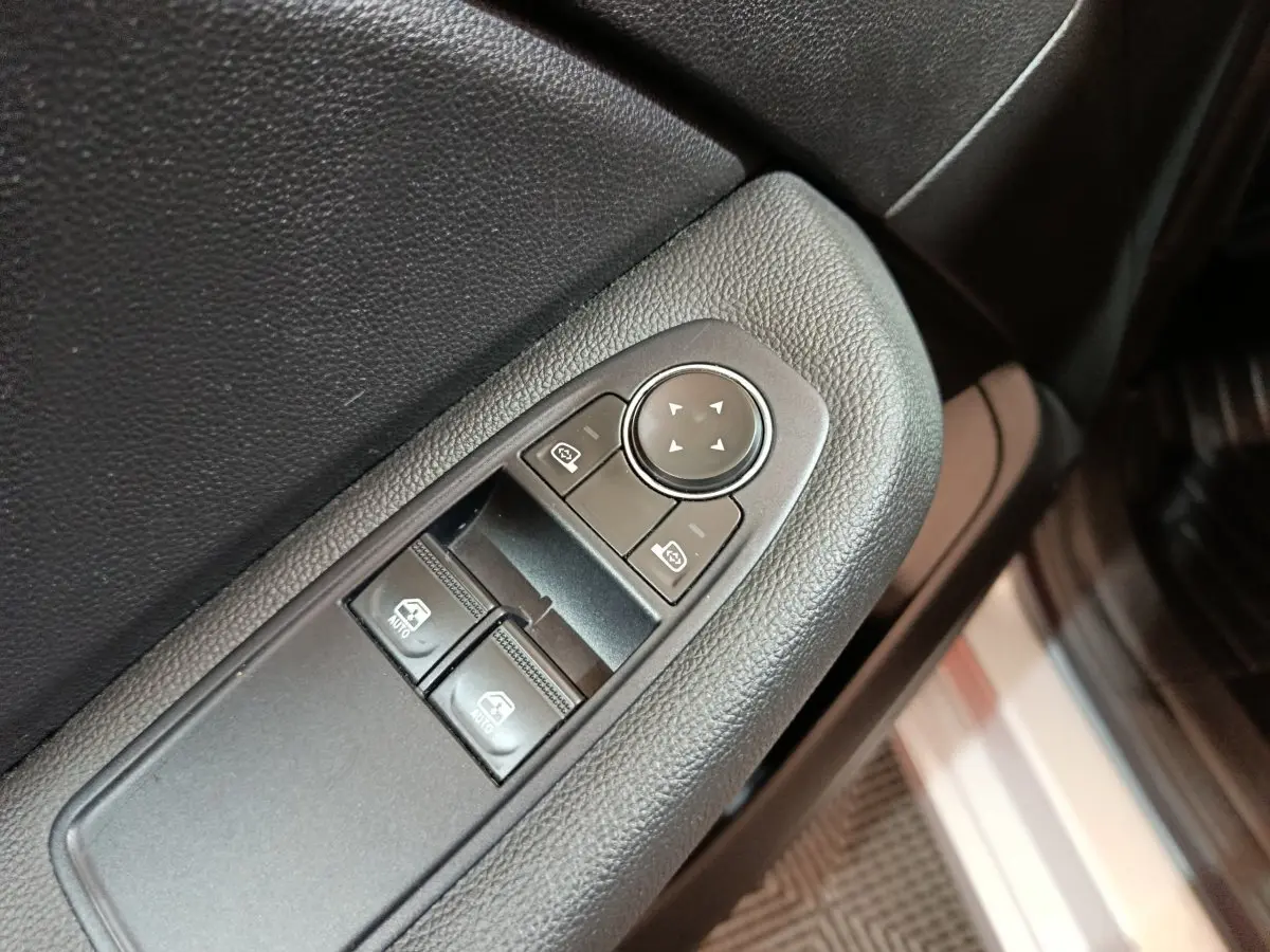 Gros plan sur les commandes de réglage des rétroviseurs et vitres côté conducteur d'une Renault Clio gris clair 2023.