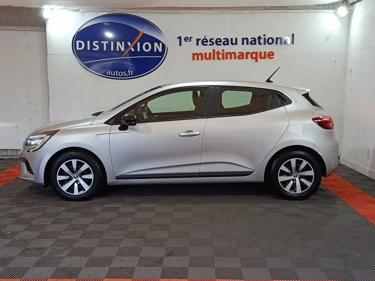 Profil droit d'une Renault Clio 2023 gris clair, avec jantes alliage et feux arrière LED visibles en intérieur showroom.