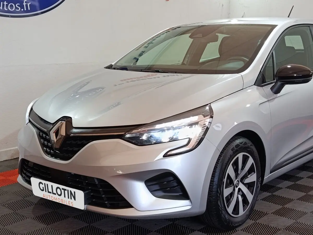 Vue 3/4 avant droite d’une Renault Clio gris clair 2023 avec phares LED et jantes distinctives.