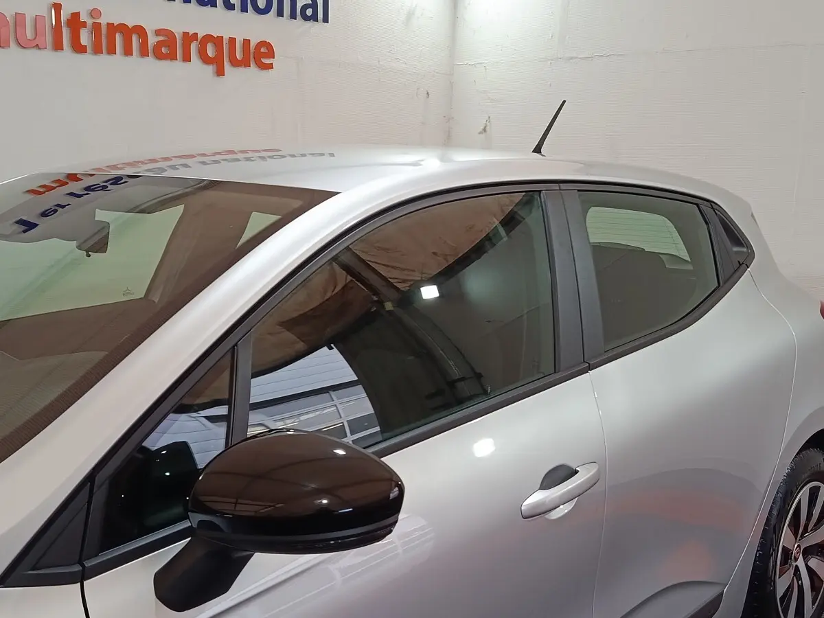 Profil droit de la Renault Clio Equilibre TCe 90 gris clair avec rétroviseur noir et jantes alliage visibles en intérieur showroom.