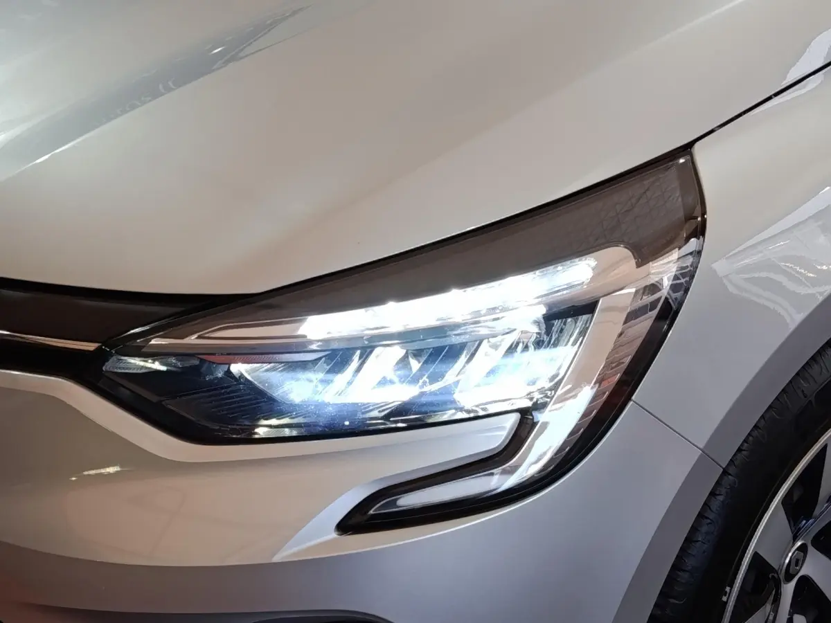 Gros plan sur le phare avant droit allumé d'une Renault Clio gris clair 2023, avec jante visible.