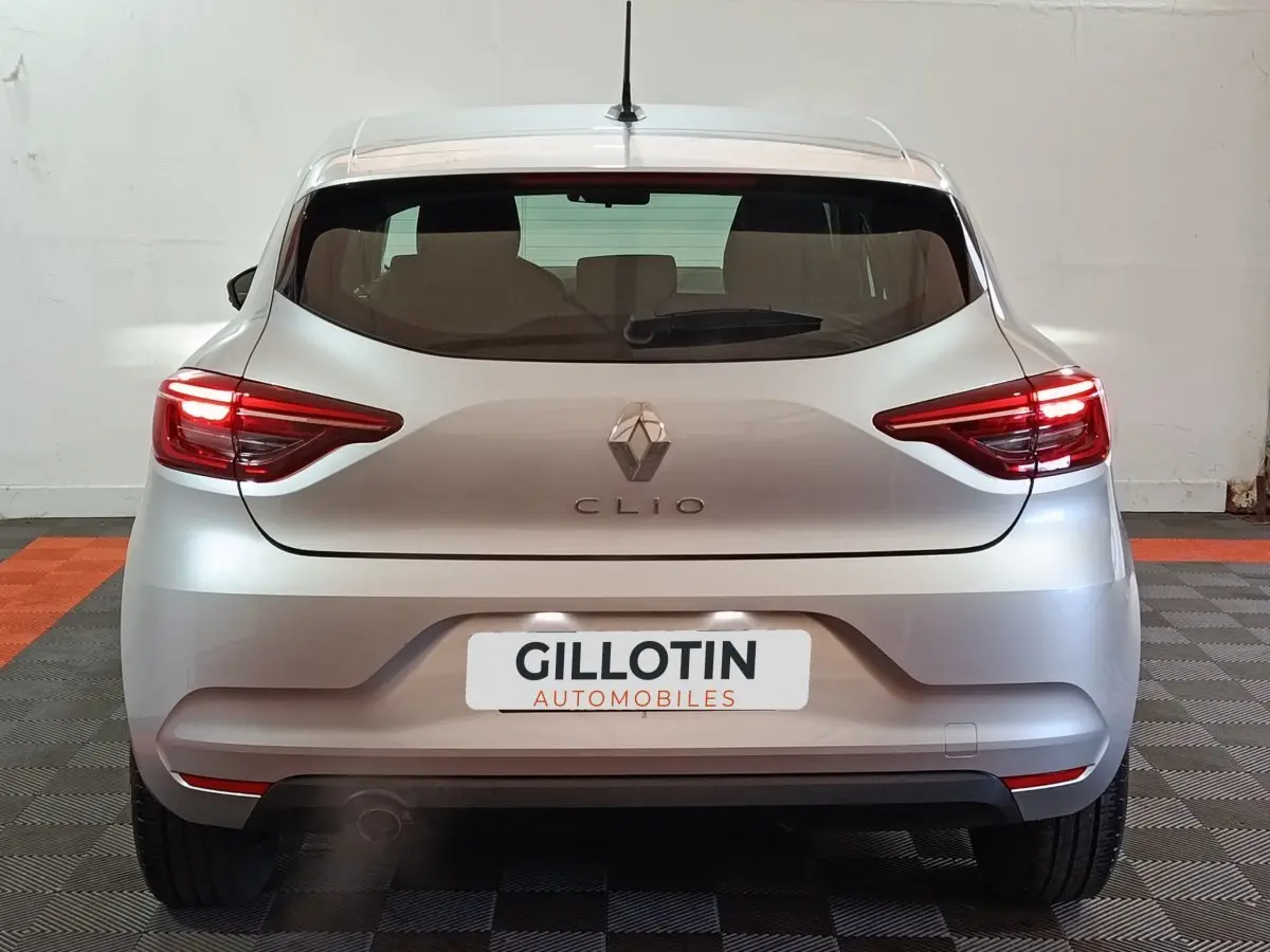 Vue arrière d'une Renault Clio gris clair 2023 avec feux LED allumés et logo centré sur le hayon.