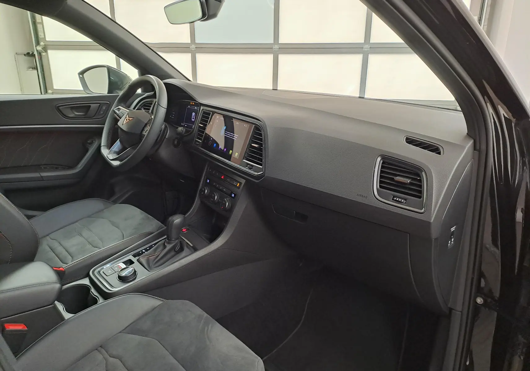 Intérieur du CUPRA Ateca 2024 noir magique, vue côté conducteur, tableau de bord moderne avec écran tactile central.