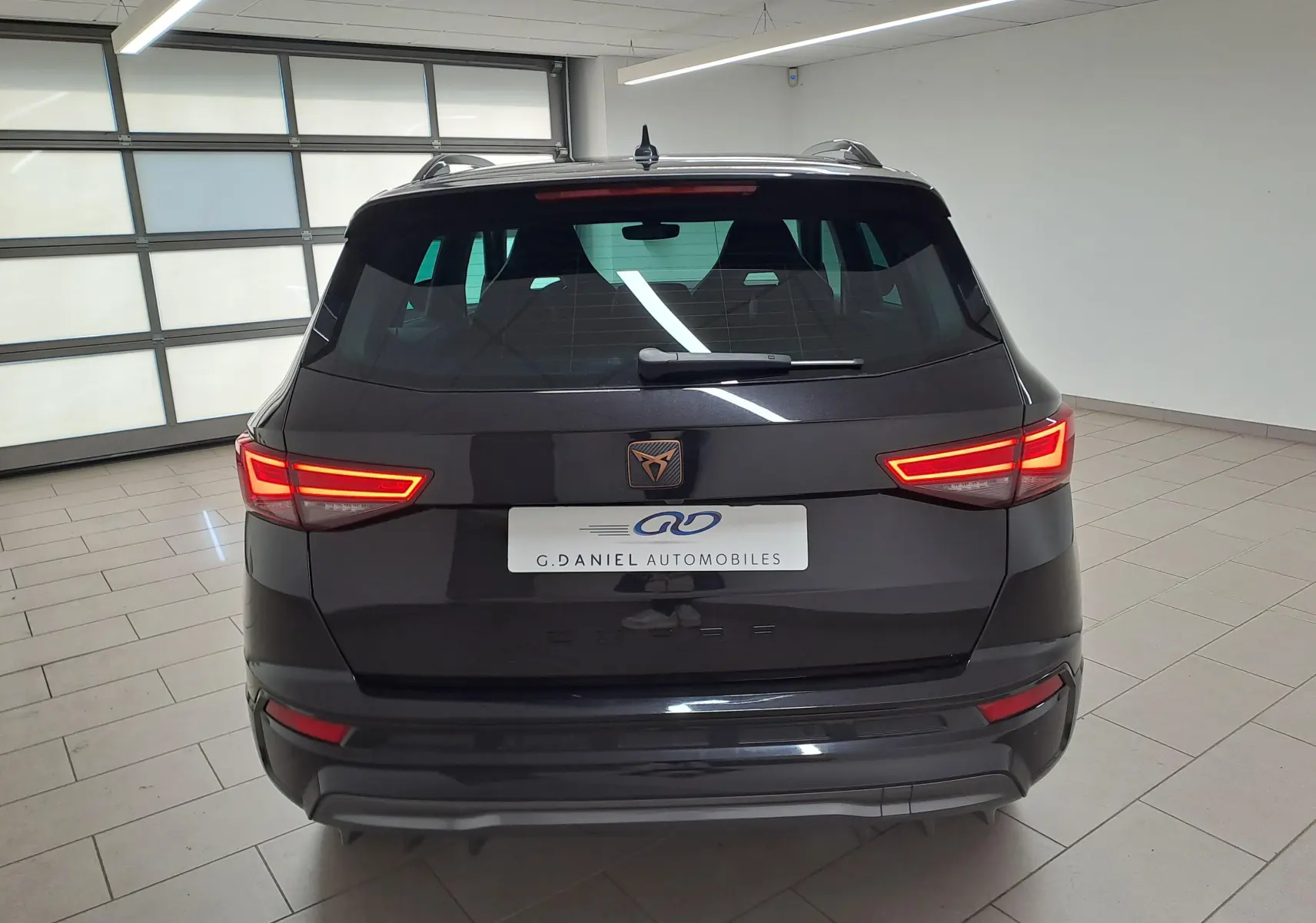 Vue arrière d’un CUPRA Ateca 2024 noir magique avec feux LED allumés dans un garage lumineux.