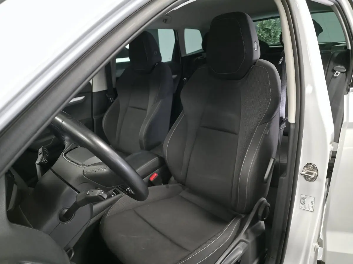 Vue intérieure côté conducteur du Skoda Karoq blanc 2024, sièges tissu noir et volant multifonctions.