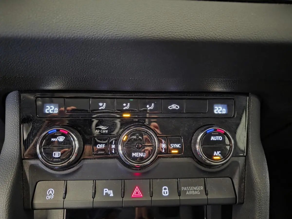 Détail de la console centrale noire avec commandes de climatisation automatique bi-zone et boutons de sécurité du Skoda Karoq blanc.
