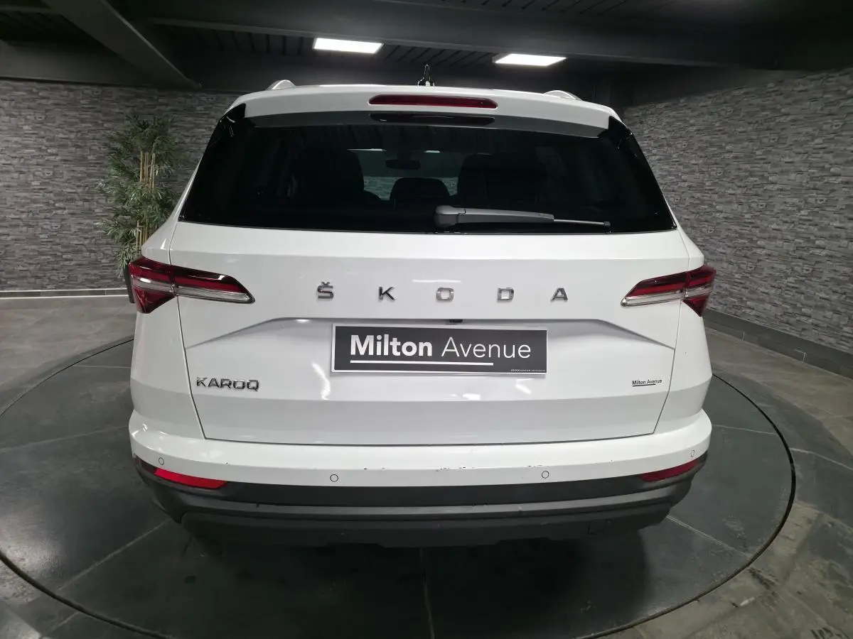Vue arrière d'un SUV SKODA KAROQ blanc 2024 avec feux arrière LED et logo ŠKODA visible sur le hayon.