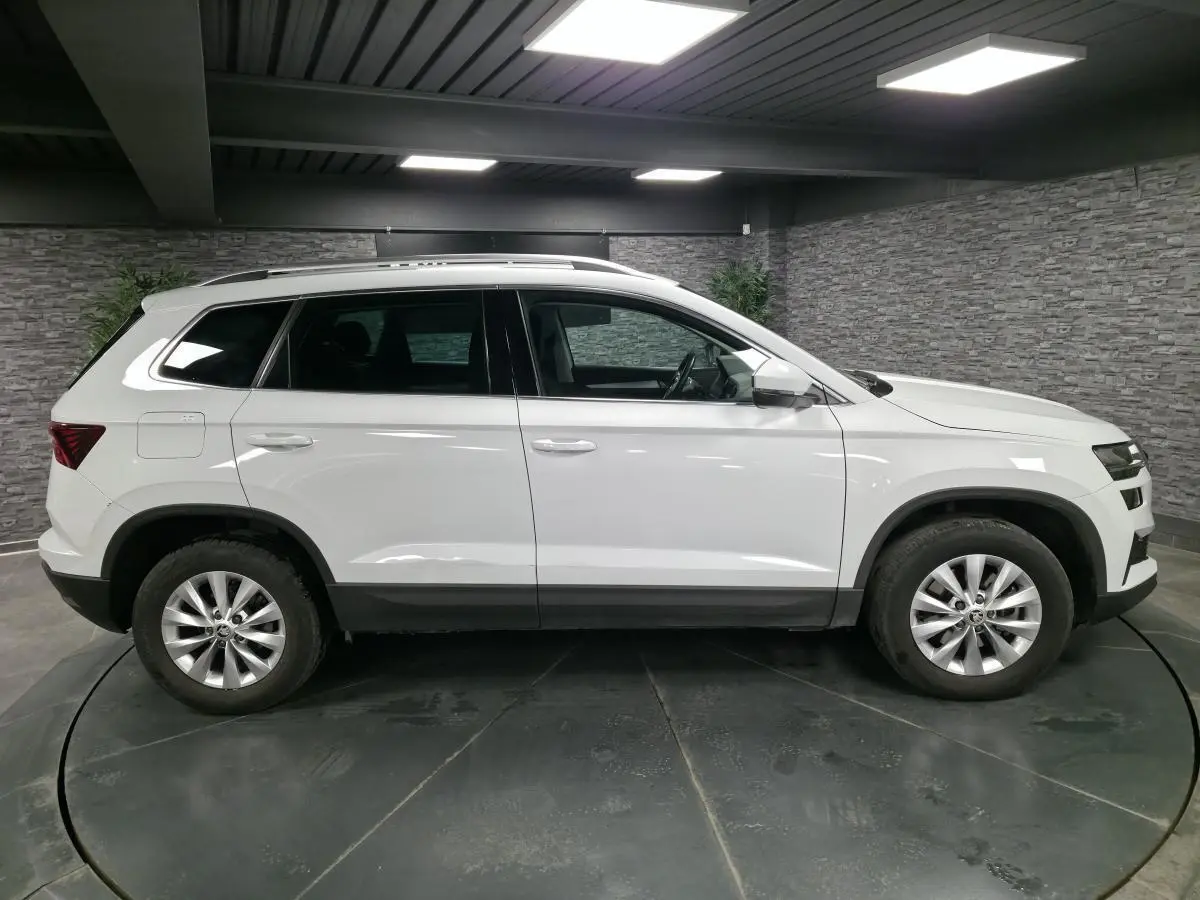 Vue latérale droite du SUV blanc Skoda Karoq 2024 avec jantes alliage et protections noires sur les passages de roues.