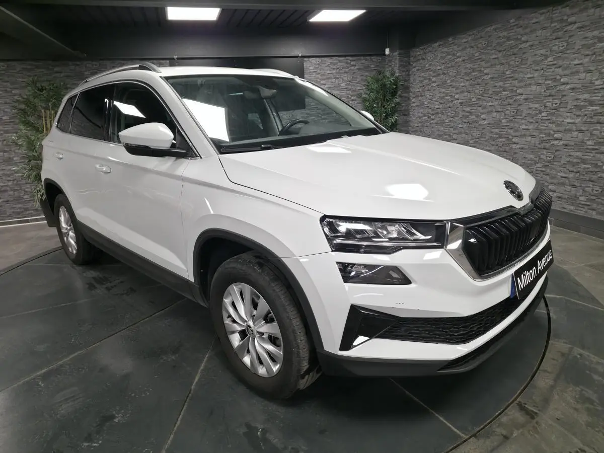 SUV Skoda Karoq blanc en 3/4 avant droit avec calandre noire et jantes alliage 16 pouces dans un showroom.