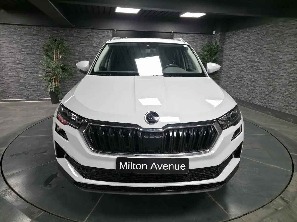 Vue frontale d'un SUV Skoda Karoq blanc 2024 avec calandre noire et plaque "Milton Avenue" en intérieur showroom.