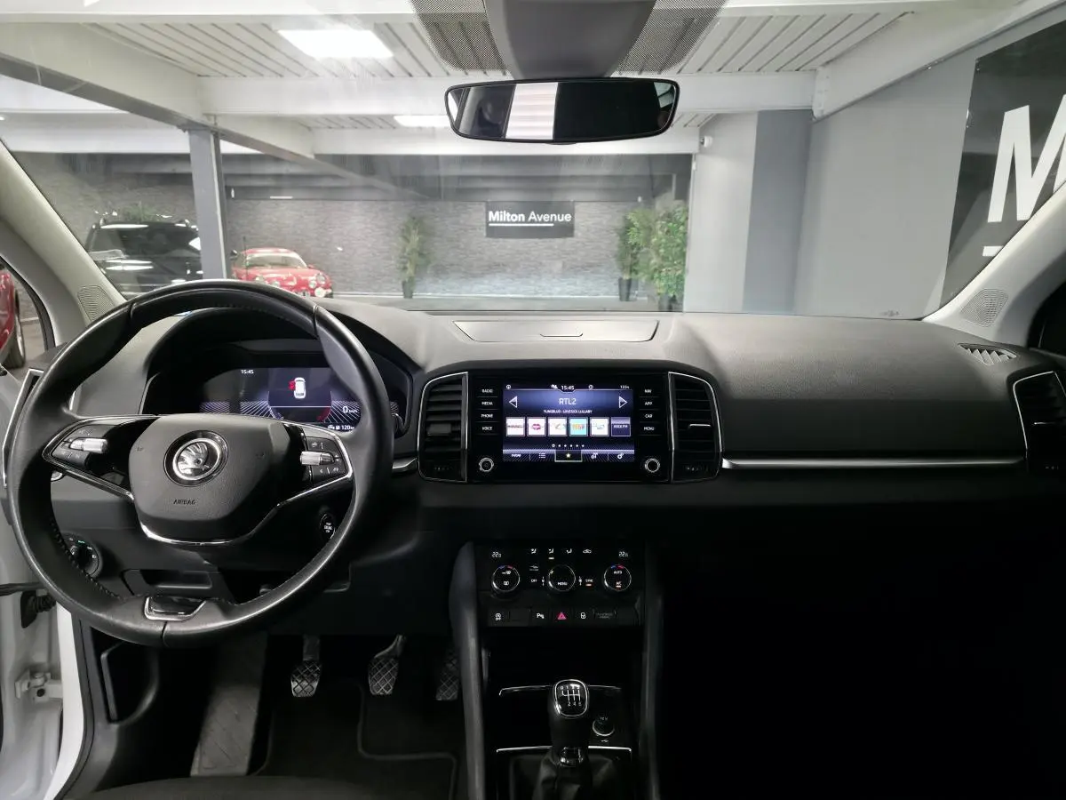 Intérieur du Skoda Karoq blanc 2024, vue frontale sur tableau de bord, volant multifonction et écran tactile central.