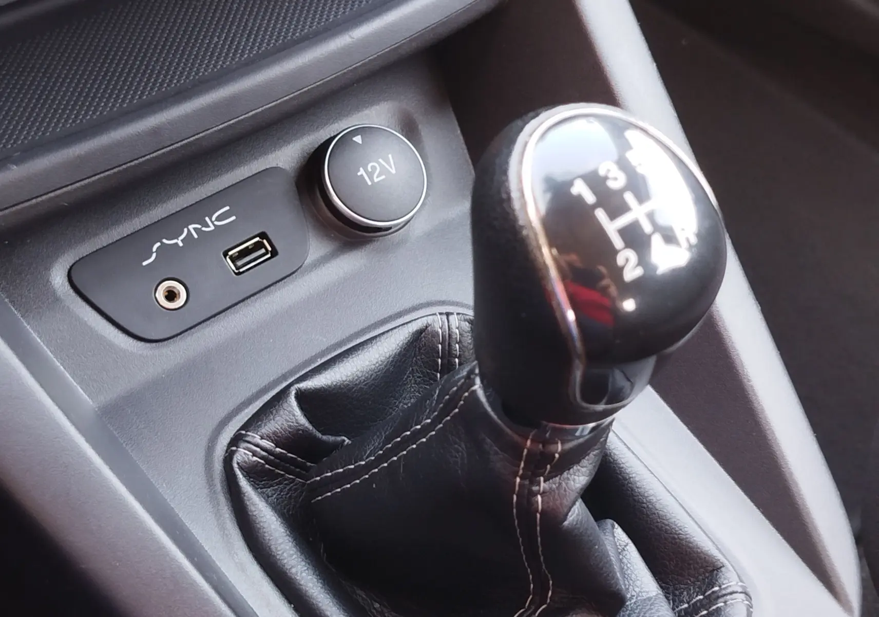 Gros plan sur le levier de vitesses manuel noir et les prises SYNC et 12V du Ford KA+ 1.2 Ti-VCT Édition Noire.