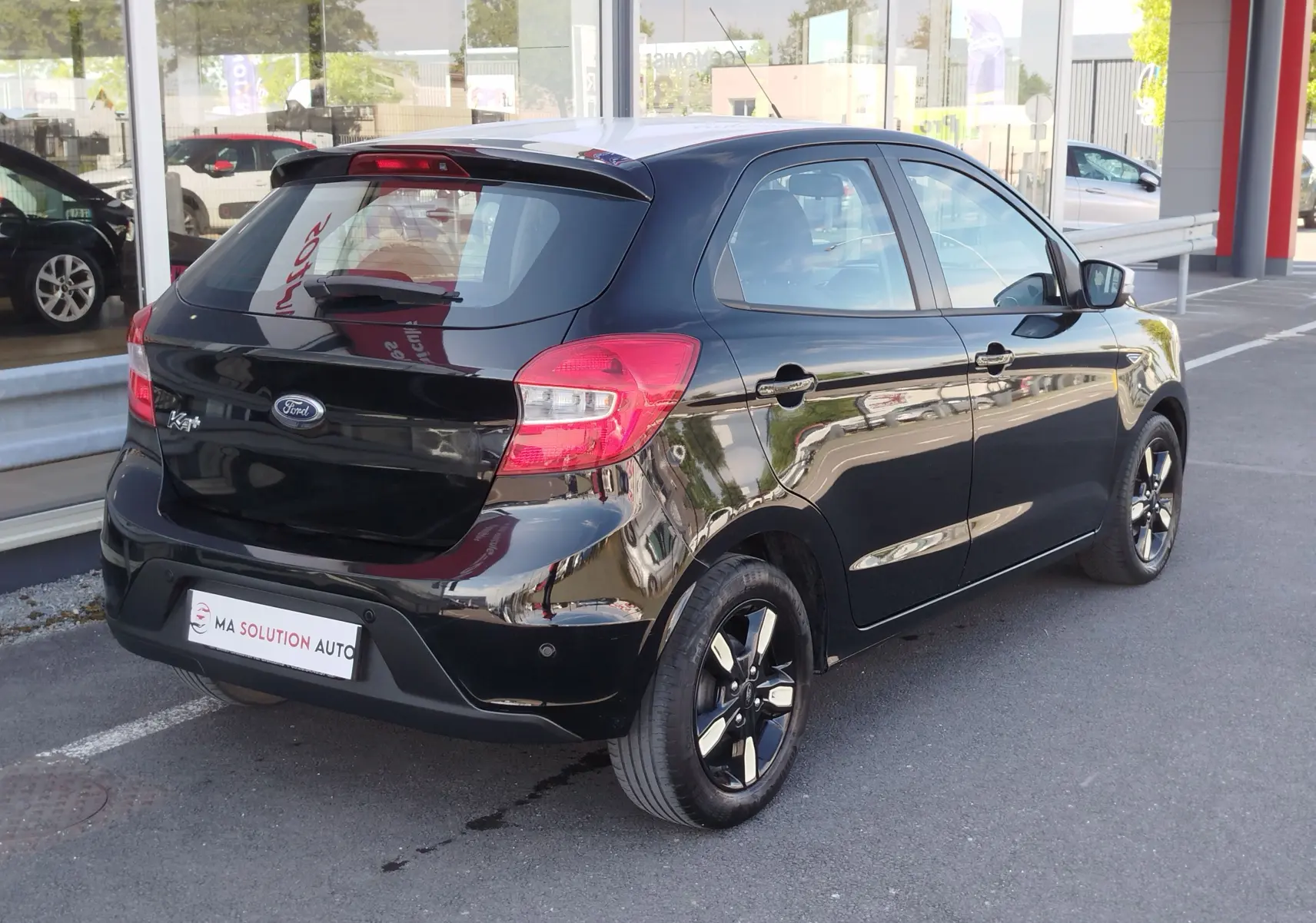 Ford Ka+ noir Shadow avec toit blanc, vue 3/4 arrière droit, jantes biton et feux arrière rouges visibles.