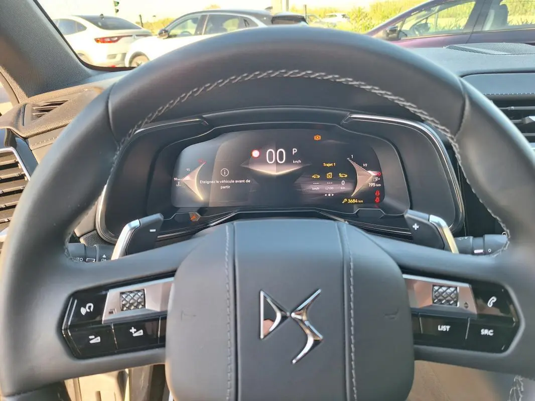 Vue intérieure centrée sur le volant DS en cuir avec tableau de bord numérique allumé du DS7 gris 2025.