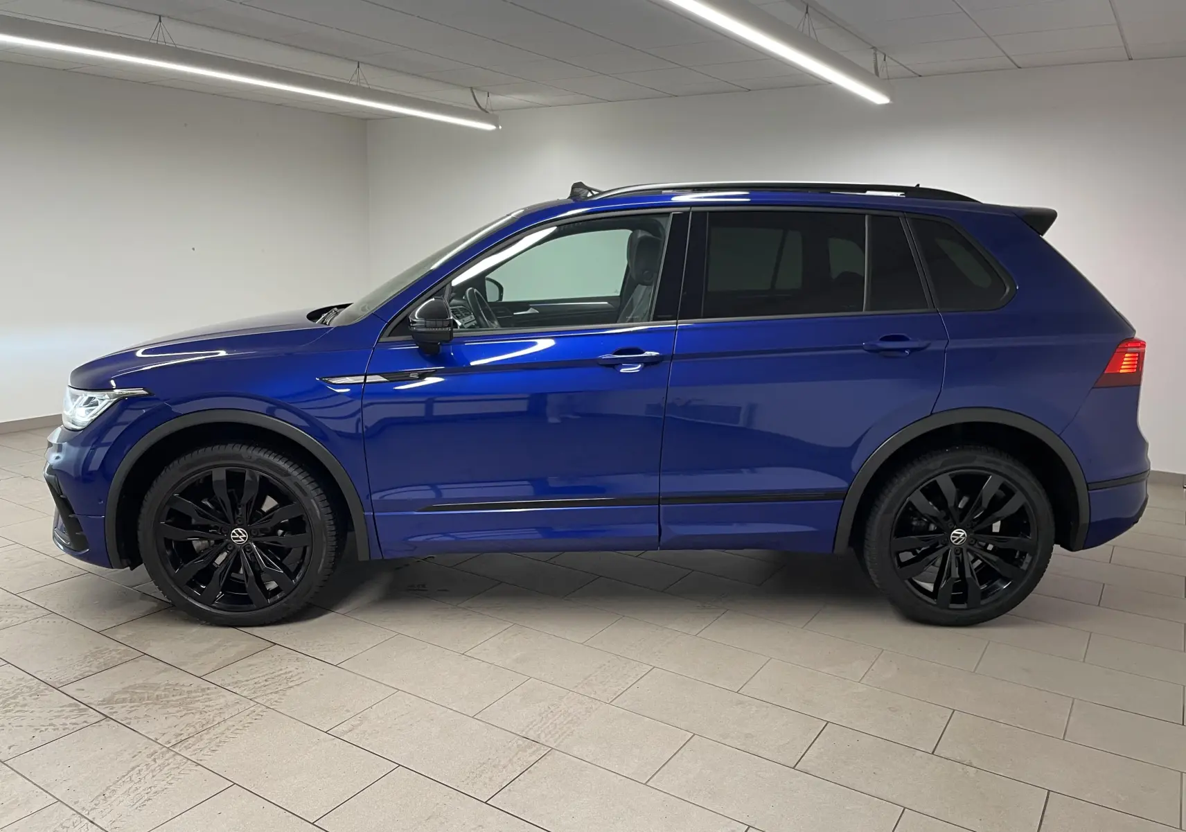 Vue de profil côté gauche d'un Volkswagen Tiguan Bleu Lapiz avec jantes noires et vitres arrière surteintées.