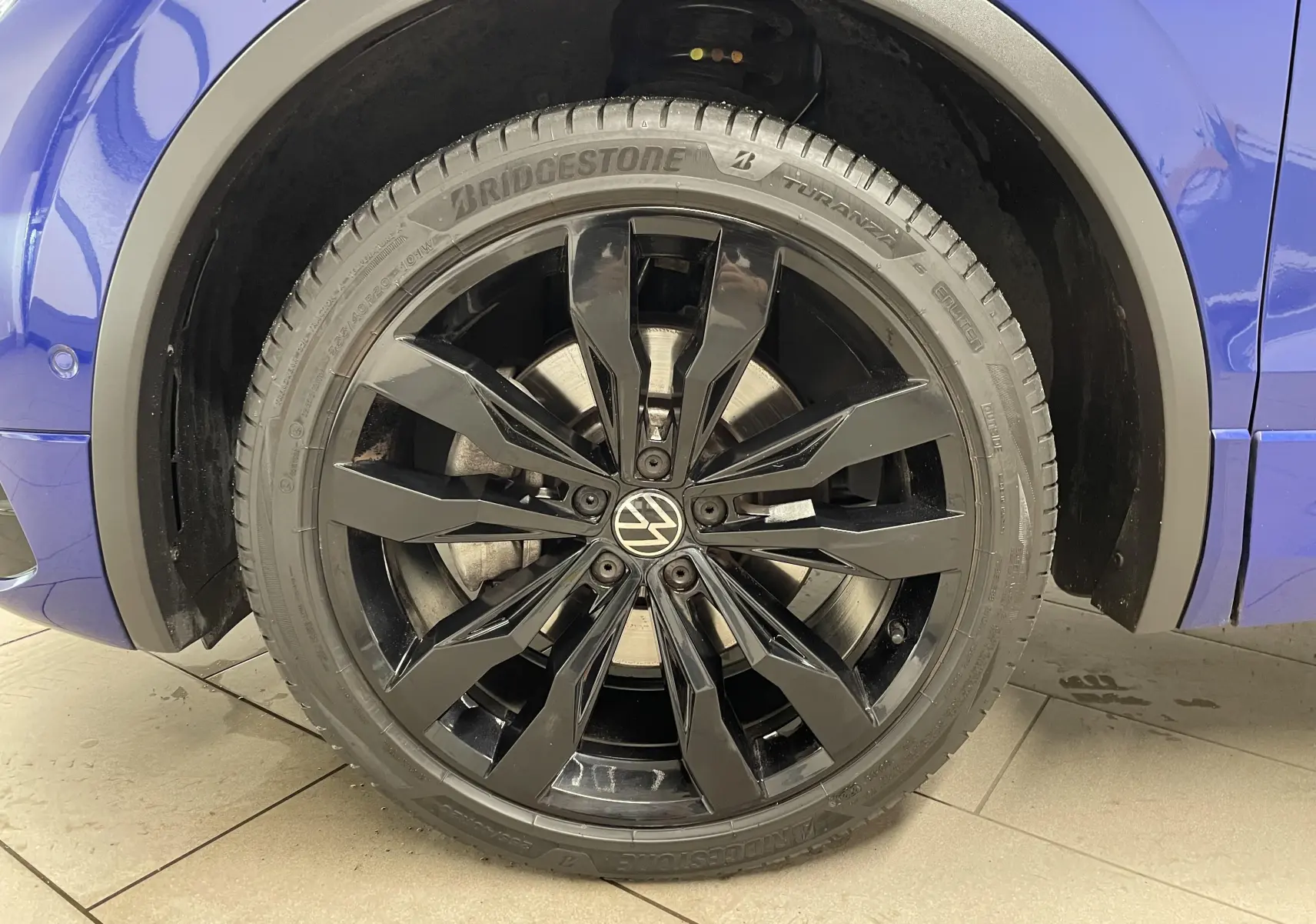 Gros plan sur la jante noire 20'' Suzuka du côté gauche d'un Volkswagen Tiguan Bleu Lapiz 2022.