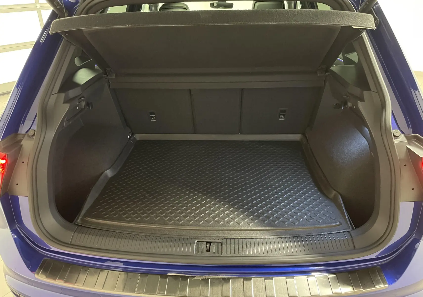 Coffre ouvert vu de l'arrière d'un Volkswagen Tiguan Bleu Lapiz, avec tapis de protection noir et seuil métallique.