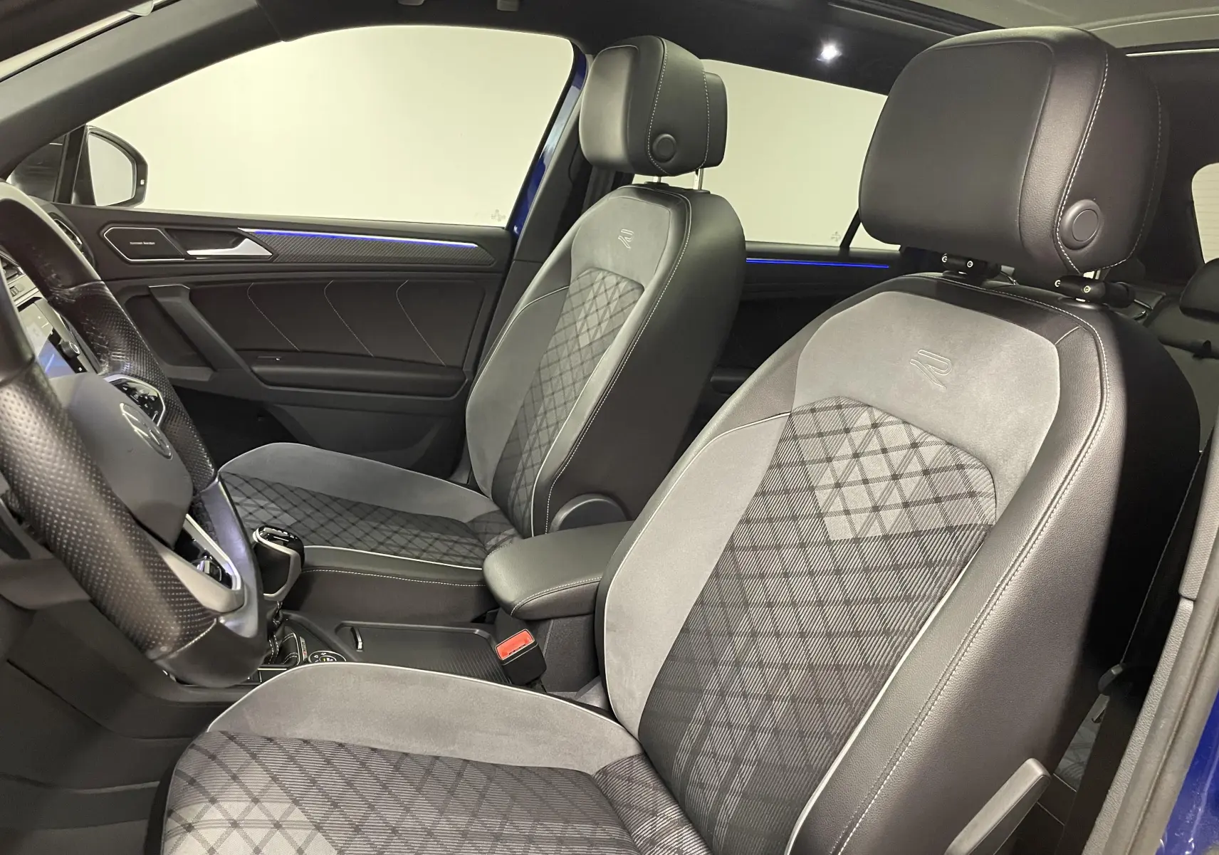 Vue intérieure côté conducteur du Volkswagen Tiguan 2022, sièges en cuir noir et alcantara avec surpiqûres blanches.