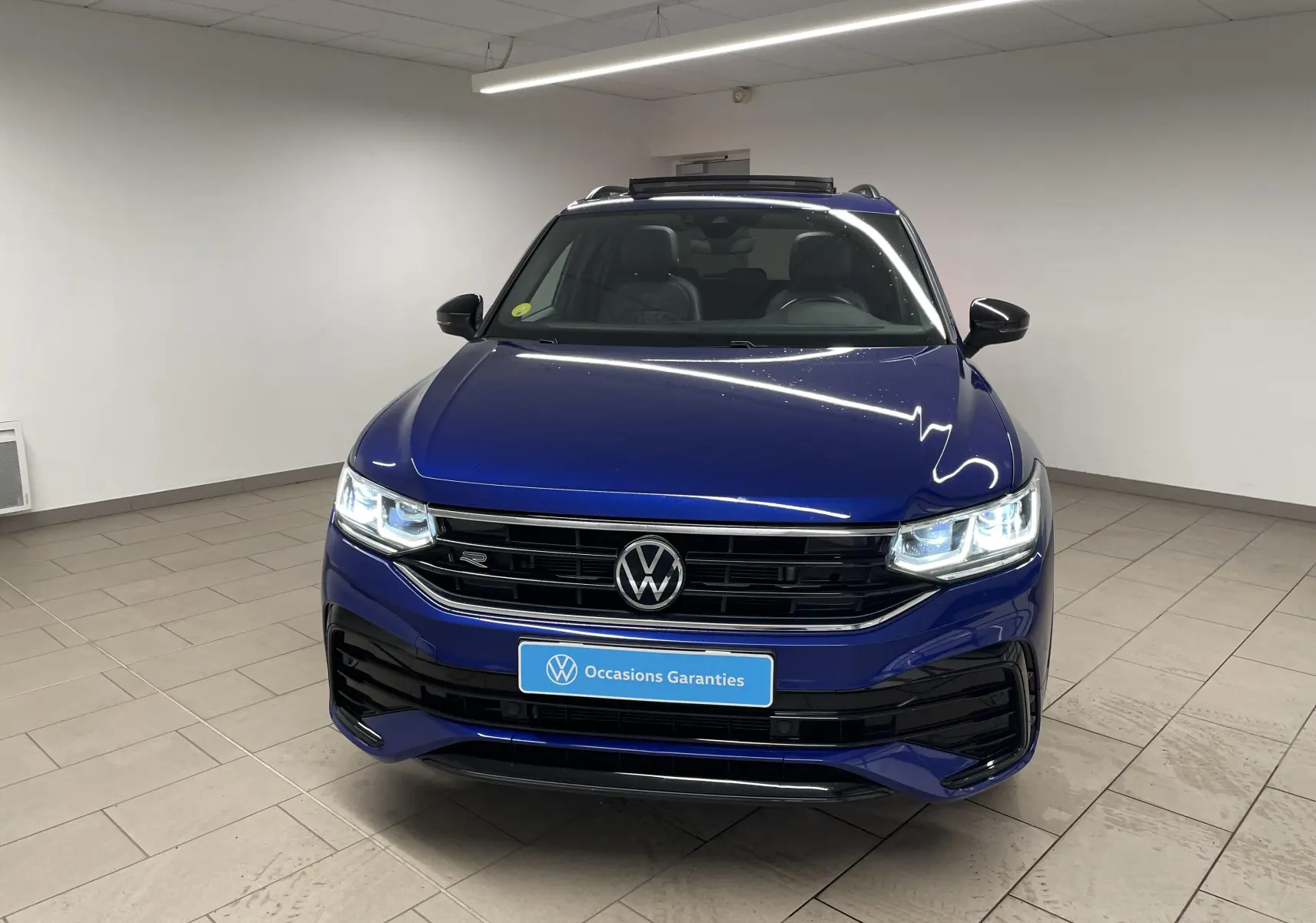 Volkswagen Tiguan Bleu Lapiz vu de face, calandre noire et projecteurs Matrix LED allumés dans un showroom.